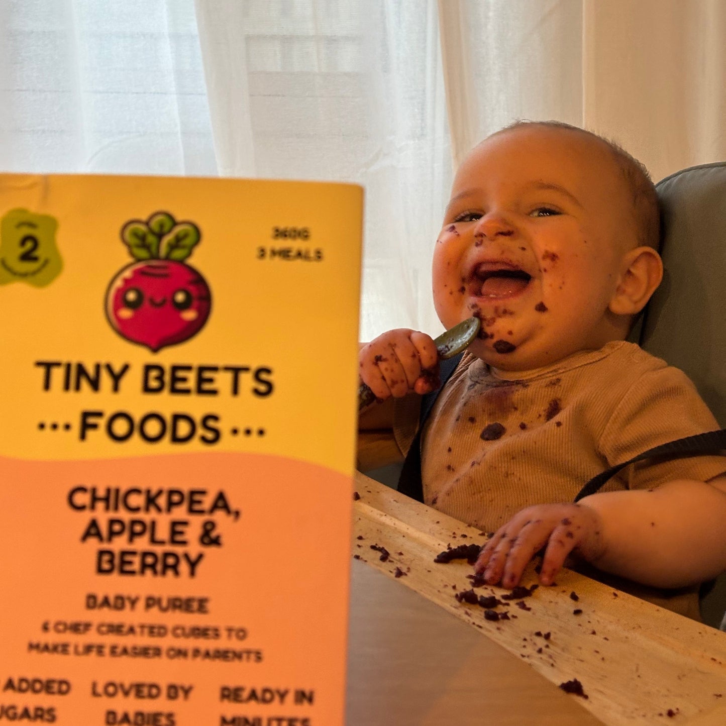 Baby eating from a box of Tiny Beets food with a spoon.