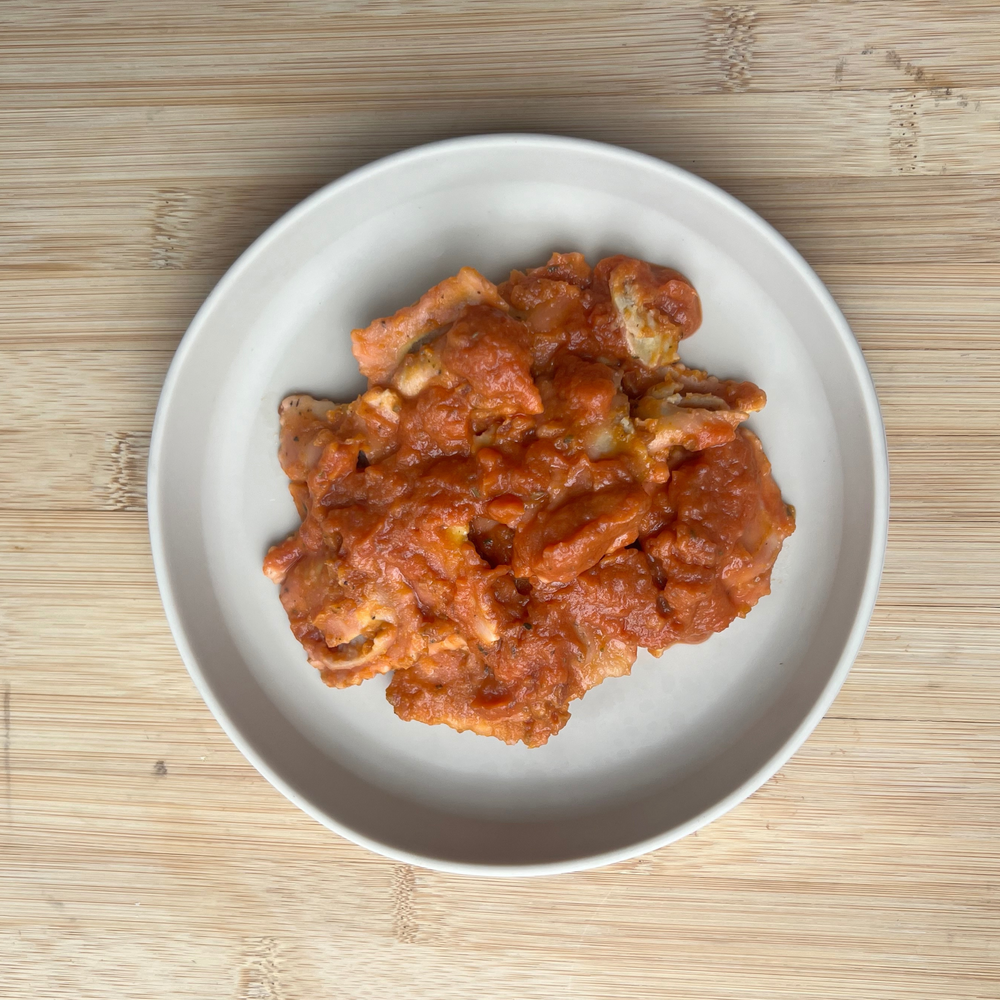 A plate filled with chicken ravioli in a rich red sauce, served on a wooden surface.