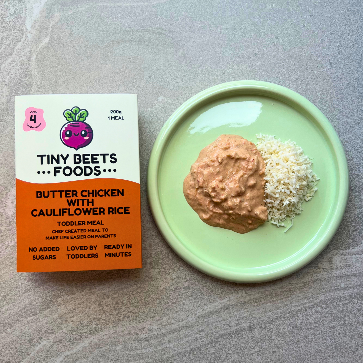 Tiny Beets Foods butter chicken with cauliflower rice packaging next to a green plate with food on a gray surface