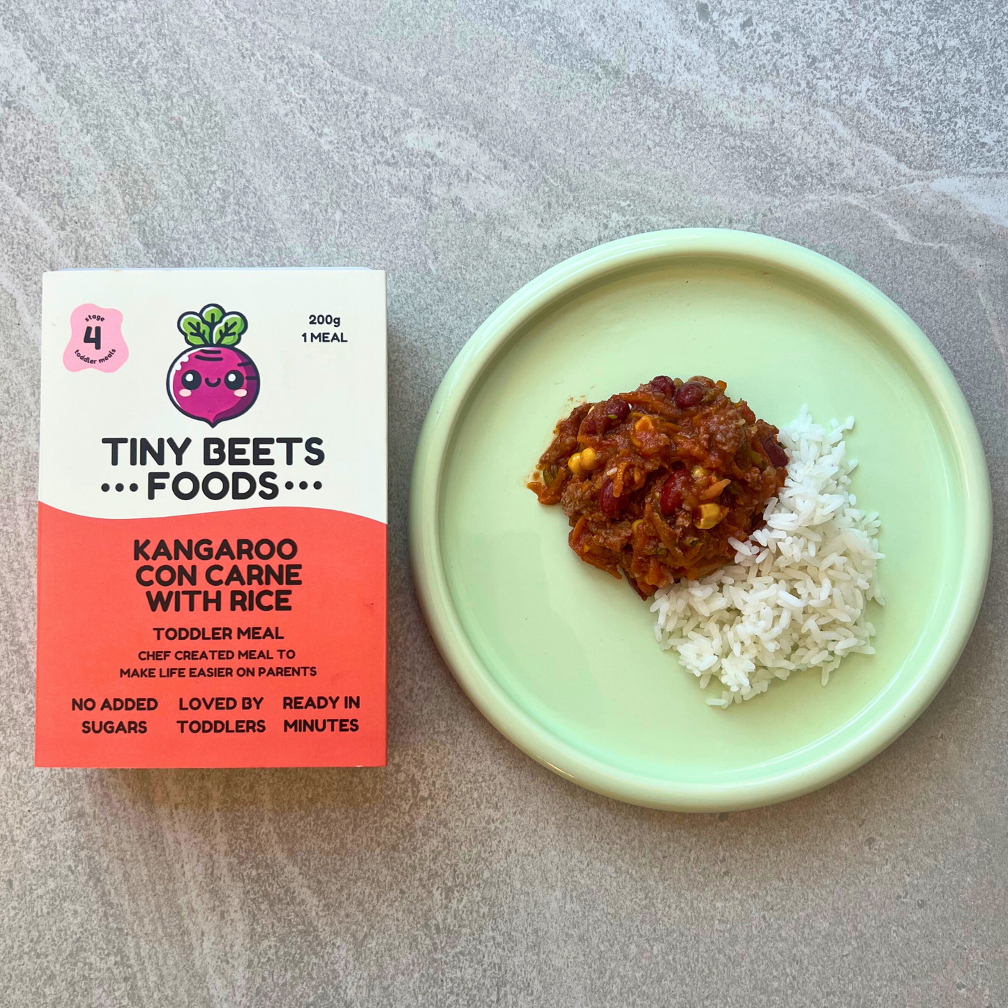 Tiny Beets Foods kangaroo con carne with rice package next to a plate of food on a gray surface