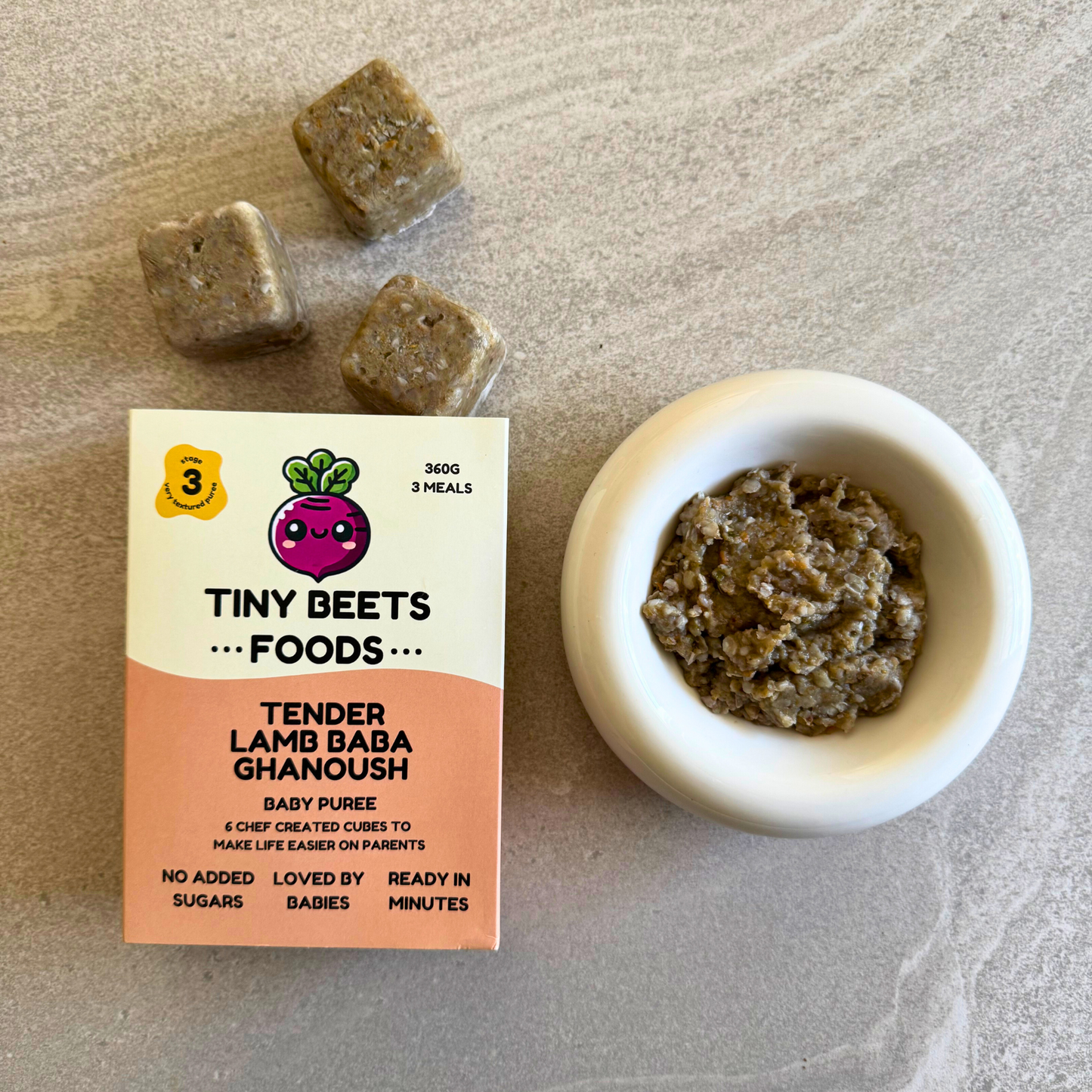 Tiny Beets Foods Tender Lamb Baba Ghanoush packaging with puree cubes and a bowl of puree on a neutral background